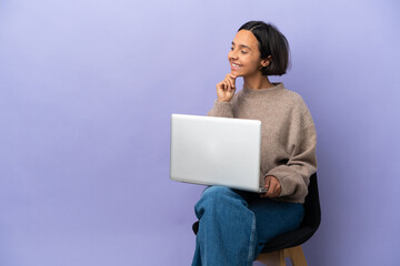 Naklejka premium Young mixed race woman sitting on a chair with laptop isolated on purple background looking to the side and smiling