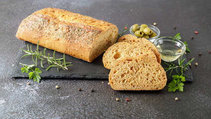 Fresh baked ciabatta bread slices with olives, herbs and spices  closeup on stone board.