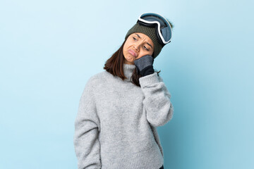 Mixed race skier girl with snowboarding glasses over isolated blue background with tired and bored expression.