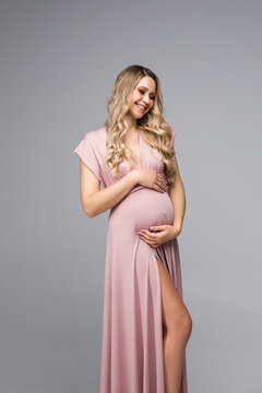 Beautiful pregnant woman in pink dress on grey background. Pregnancy woman. Vertical photo. Pink close. Smiling pregnancy woman.