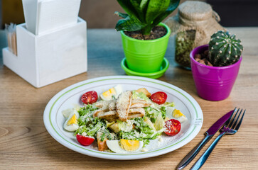 Salad with chicken on a wooden table. Caesar salad. Healthy salad made of baked turkey breast, romaine lettuce, cherry tomatoes, quail eggs, croutons, parmesan and thyme olive oil. 