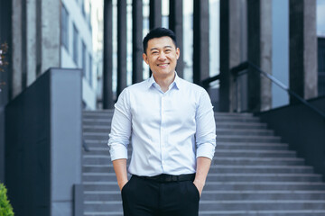 Happy asian in shirt outside near office, portrait of successful businessman, looking at camera and smiling