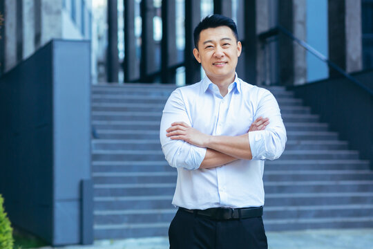 Happy asian in shirt outside near office, portrait of successful businessman, looking at camera and smiling