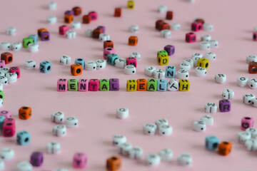 Mental health words are written in different color blocks placed on a pink surface