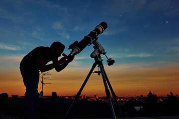 Silhouette of a man, telescope and countryside under the starry skies. © astrosystem