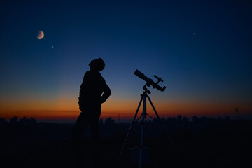 Silhouette of a man and telescope under the starry skies.