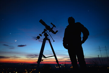 Silhouette of a man, telescope and countryside under the starry