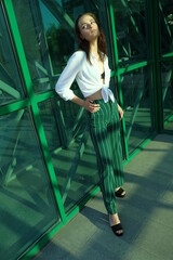 Portrait of a young brunette girl in white shirt and striped green trouser against city architecture
