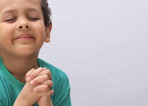 boy praying to God with hands held together with closed eyes on white background stock photo