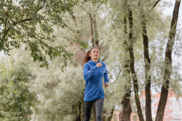 a European woman in a blue hoodie is running and doing sports in the park. fitness and yoga outdoor sports, exercise and meditation and fitness for body health. spiritual development. outdoor sports