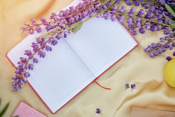 Open notebook mock up with purple lupins flowers golden background. Summer picnic. Copy space. Closeness to nature, self-discovery concept.