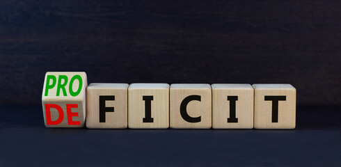 Proficit or deficit symbol. Turned wooden cubes and changed the concept word deficit to proficit. Beautiful black table black background. Business, proficit or deficit concept. Copy space.