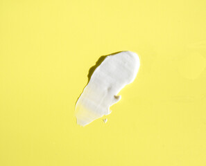 White smear of cosmetic cream on a yellow background. Creamy base texture isolated. A smear of face cream. Close-up of creamy texture