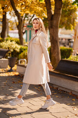 beautiful blonde student or businesswoman in a coat walks down an autumn street.