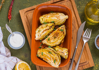 Fresh young cabbage baked in pieces in the oven with spices and olive oil in a ceramic form on a green concrete background. Vegan food. Vegetable recipes