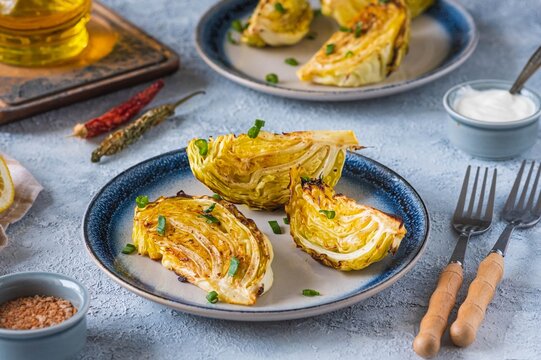 Fresh young cabbage baked in pieces in the oven with spices and olive oil on a ceramic plate on a light concrete background. Vegan food. Vegetable recipes