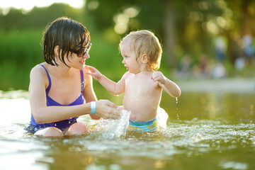 Cute toddler boy and his big teenage sister playing by a river on hot summer day. Adorable child...