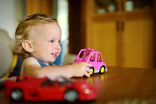 Cute toddler boy playing with colourful toy cars at home.
