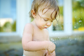 Adorable toddler boy playing with a garden hose on warm summer day.