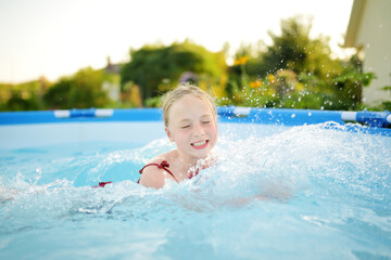 Cute young girl having fun in outdoor pool. Child learning to swim. Kid having fun with water toys. Family fun in a pool.