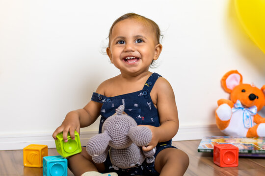 adorable 12 month old baby smiling, sitting among toys, photographed indoors	