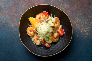 salad caesar with shrimps on black bowl on blue concrete table top view