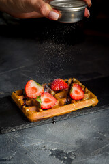 waffles with fresh strawberries and powdered sugar on grey stone table vertical