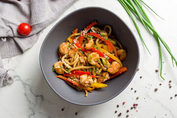 Udon wok with shrimps and vegetables top view on white marble table