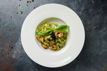 Pasta fettuccine with shrimps and pesto sauce on dark stone table top view