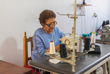 Fototapeta na wymiar Latin seamstress sitting on her workspace using a sewing machine