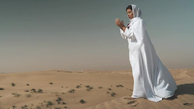 Arabic woman wearing white abaya and shayla praying in the desert