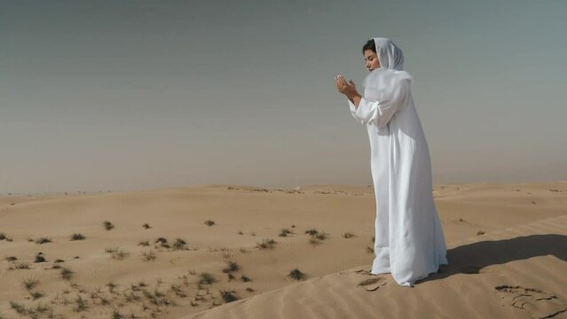Arabic woman wearing white abaya praying  in the desert