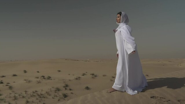 Arabic woman wearing white abaya in the desert enjoying the wind