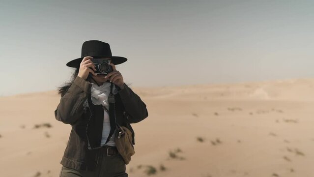 Arabic female traveler taking photos with film camera in the desert