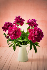 Purple  peonies in a white enamel jug on a pink wooden background, rustic style
