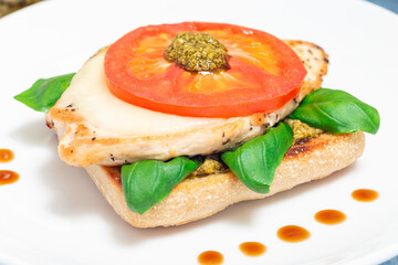 Sandwich with chicken, mozzarella, tomato, pesto and basil on toasted ciabatta, horizontal