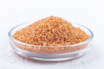Brown sugar crystals or cane sugar in bowl on white background, horizontal