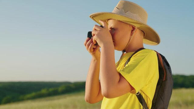 Child dreams of traveling, making discoveries. Children's fantasy in nature. Happy boy, child dreams of becoming photographer. Boy plays with camera, takes pictures of landscape in summer park.