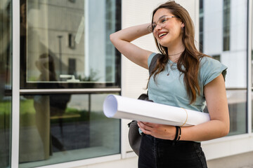 One woman young adult caucasian female student standing in front of university with paper and cup of coffee outdoor in bright day happy smile looking to the side real people copy space