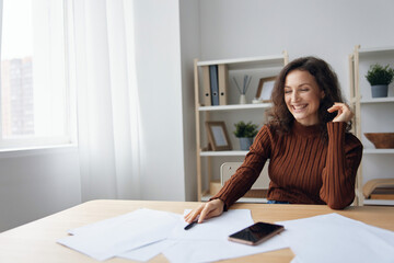Cheerful happy smiling curly woman writing script counts taxes calculates budget for purchases...
