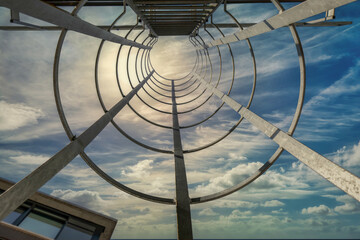 View looking up through a metal hoop style fire escape in daytime, colourful cloudy sky, nobody