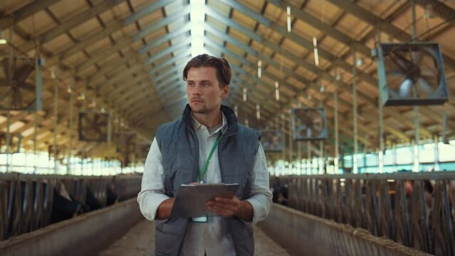 Livestock owner checking animal feedlots making notes on clipboard at cowshed.