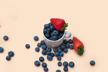 scattered delicious strawberries and blueberries in a white cup, on a beige background. top view