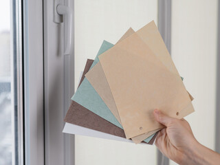 Woman holding fabric samples of roller blinds against window background. 