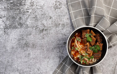 Spicy beef noodle soup or ramen with herbs in bowl on a dark gray background. Top view, flat lay