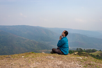 Naklejka na ściany i meble man meditating at hill top with misty mountain rage background from flat angle