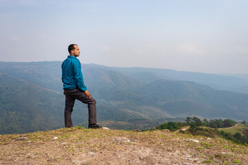 Naklejka premium man standing alone at hill top with misty mountain rage background from flat angle