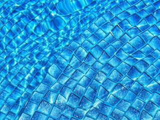 Overhead view of ripple surface water in blue swimming pool with many tiles at bootom.Swimming pool bottom caustics ripple and flow with waves background. Summer background. Texture of water surface.