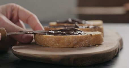 man spreading chocolate spread on ciabatta slice on olive board