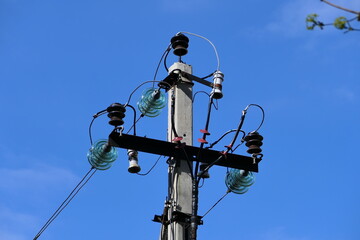 Close-up of high-voltage power lines and power pylons against a blue sky.